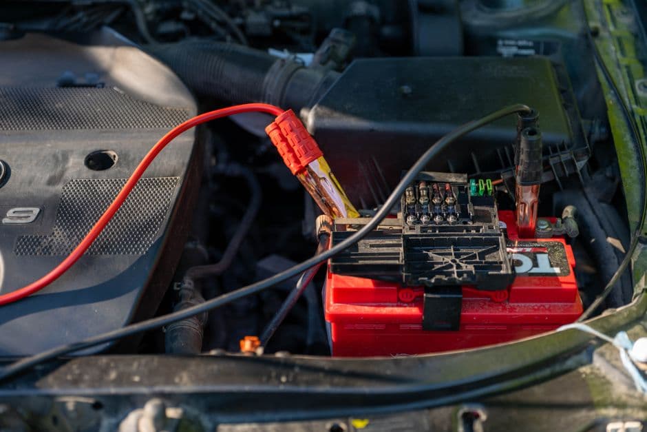 A car battery under an open hood with test leads attached