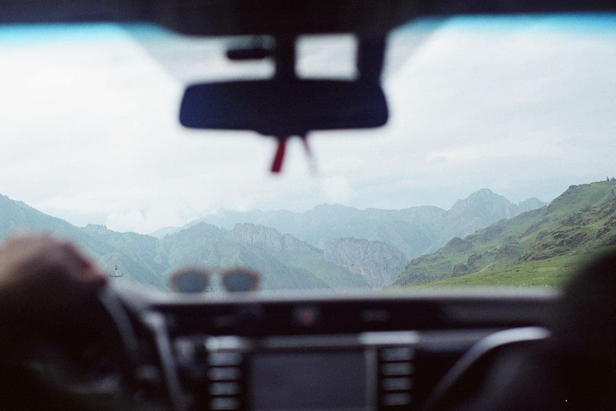 The view forward through a car windshield on a clear road, from behind the mirror