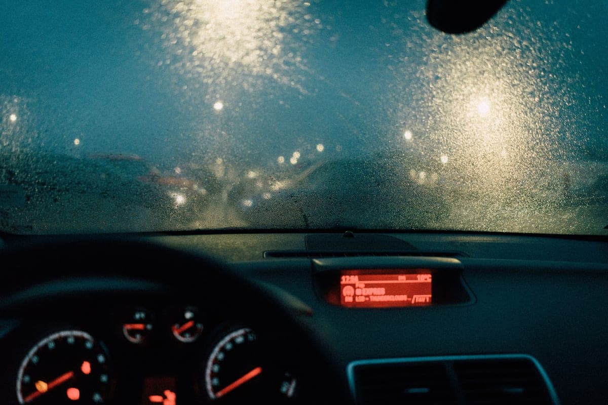 Rain on a car windshield with the road ahead blurred through the glass