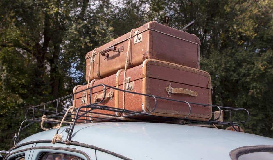 A loaded car on a road with luggage secured on the roof