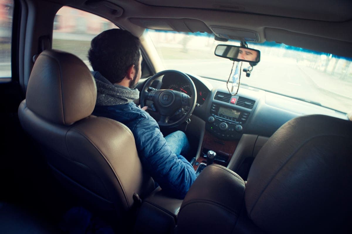 A driver seated in a car with hands on the steering wheel on a long road