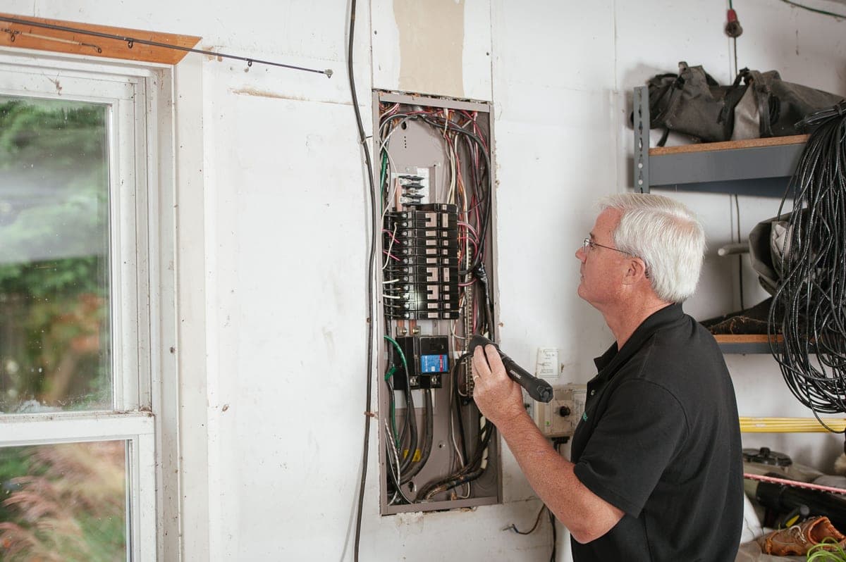 A pair of hands working at an open fuse box panel inside a car footwell