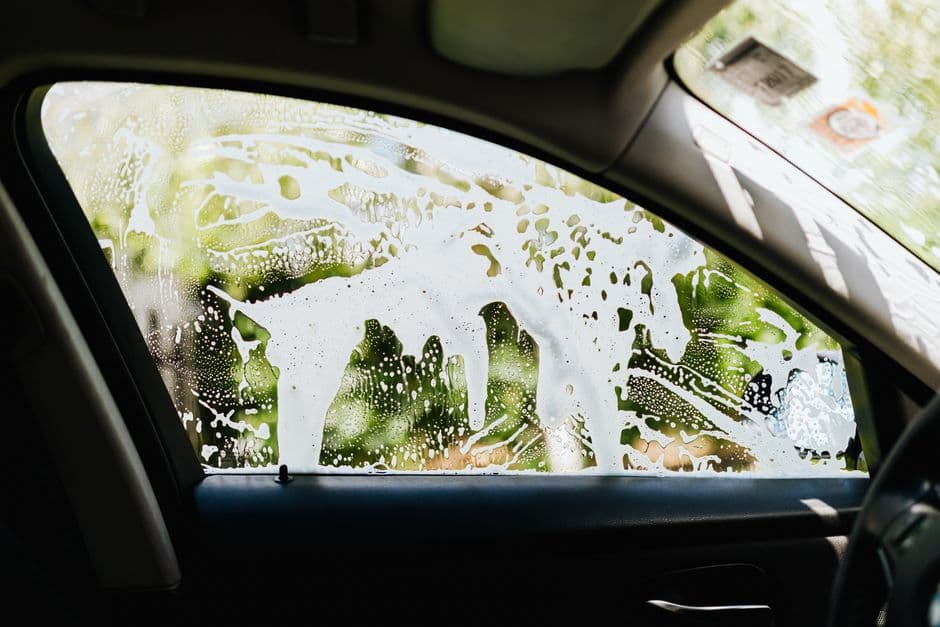 A hand cleaning the inside of a car windshield with a cloth
