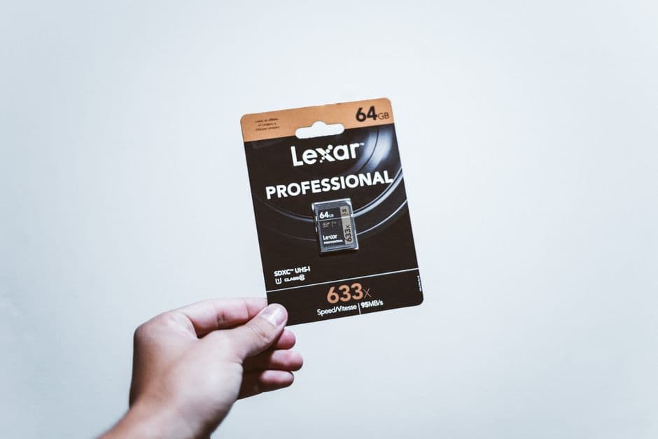 A hand holding a small memory card beside a laptop