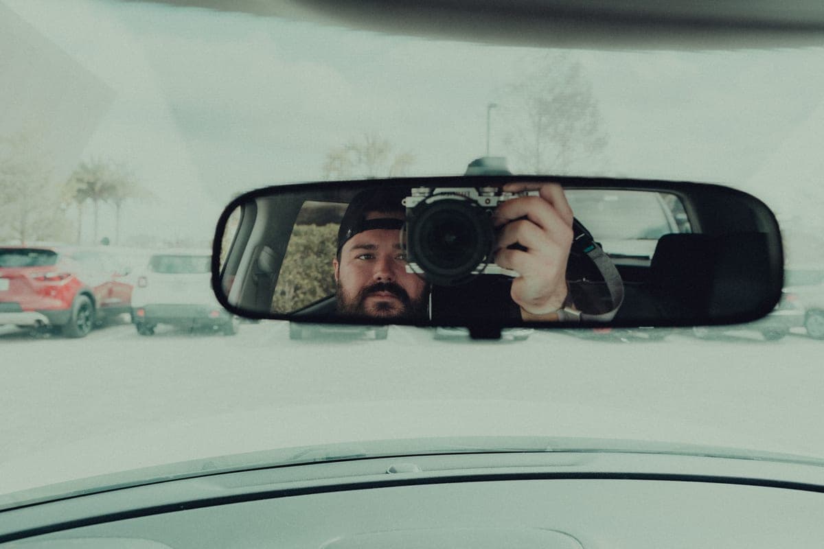 A small dash camera mounted behind a car's rear-view mirror against the windshield